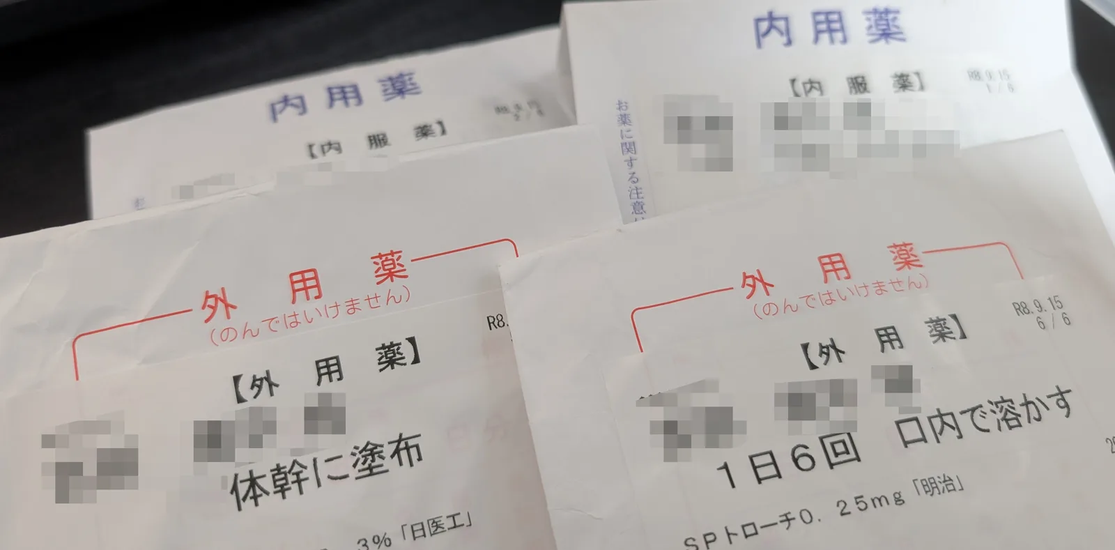 薬袋が 4 つ重なっている。奥の 2 つには青い字で「内用薬」、手前の 2 つには赤い字で「外用薬 (のんではいけません)」と刷ってある。手前の左の袋には「体幹に塗布」、右の袋には「1 日 6 回 口内で溶かす」と SP トローチの名前が印字されている